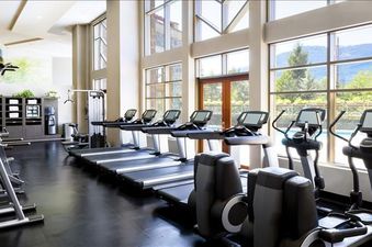 A wide, bright gym with modern exercise equipment, large windows, and a scenic mountain view.