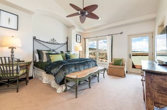 The bedroom in Peaks Penthouse 846 features a large bed with a dark green comforter and light green pillows, a wrought iron headboard, and a ceiling fan.