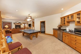 A spacious recreation room featuring a ping pong table, a cozy living area with a fireplace, and a wet bar.