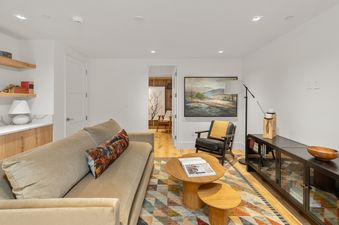 A modern living room at Depot Place with a light brown sofa, a colorful geometric rug, and a black armchair, all under recessed lighting.