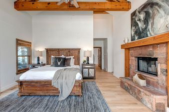 A cozy bedroom with a king-size bed, a fireplace, and a large window with a view of the mountains.
