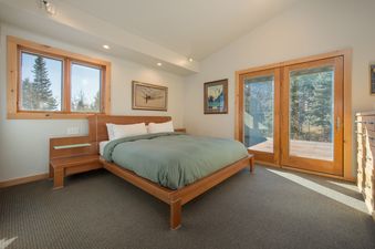 A bright bedroom at Westbrook House with a queen-size bed, wooden finishes, and large glass doors leading to an outdoor deck.
