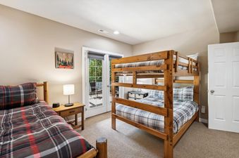 A cozy children's bedroom at Bitterroot Escape featuring a wooden bunk bed and a single bed, both adorned with plaid bedding, and French doors leading to an outdoor patio.