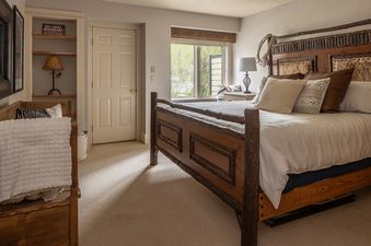 A rustic bedroom with a large wooden bed, a window overlooking greenery, and a built-in shelf.