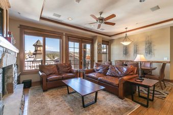 A living room with a fireplace, two couches, a coffee table, and a large window with a view of a snowy mountain town.