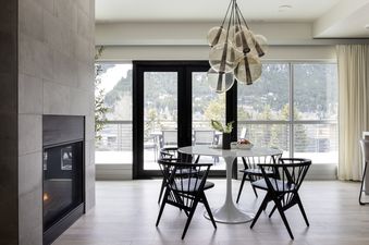 A modern dining area in Penthouse on Glenwood 401 with a white tulip table, black chairs, a glass orb chandelier, and large windows offering a snowy mountain view.