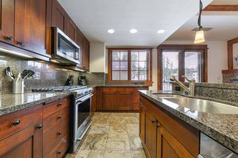 The kitchen of Big Horn Lodge 202 features modern stainless steel appliances and a granite countertop, with wooden cabinets surrounding the space and a large window offering a view of the outdoors.
