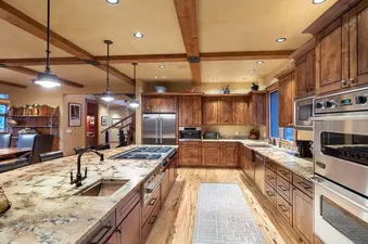 A modern kitchen with stainless steel appliances, a large granite countertop island, and wooden cabinets.