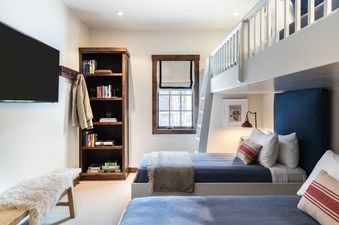 A cozy bunk bedroom at Four Pines 07 features two bunk beds with blue bedding, a bookshelf, a flat-screen TV, and a window with a Roman shade.
