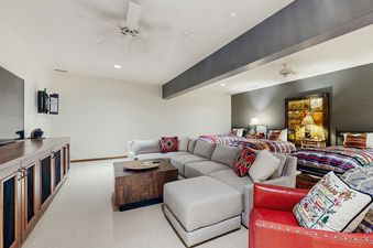 A large L-shaped sectional sofa faces a media console with a TV, with two twin beds visible in the background.