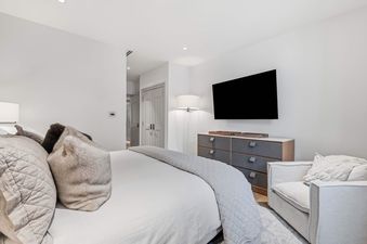 The Solaris 5F East bedroom, showcasing a comfortable bed with plush pillows and a quilted throw, a modern dresser with a mounted TV, and an elegant armchair.
