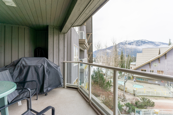 The outdoor balcony features a covered BBQ grill and patio furniture, with a view of a pool area and mountains in the distance.