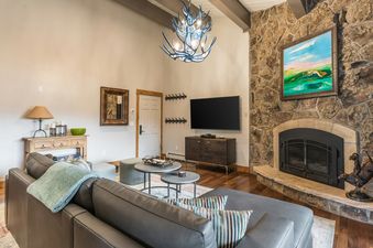 The living area of Phoenix 120 features a gray leather sectional sofa, a large stone fireplace, and a unique antler-style chandelier.
