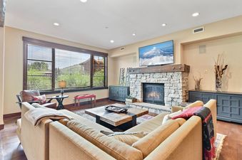A living room with a large sectional couch, a fireplace, and a TV playing a snowy mountain scene.