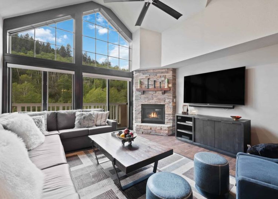 A spacious living room at St James Place 437 featuring a large L-shaped sofa, a stone fireplace, a flat-screen TV, and floor-to-ceiling windows with mountain views.