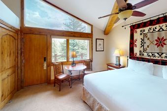 The spacious bedroom in Manor Vail 339 has a king-size bed, a window with a view of the trees, and a separate sitting area with two chairs and a table.