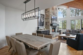 Open-plan dining and living area in Twin Pines 5 featuring a large wooden table and a stone fireplace.