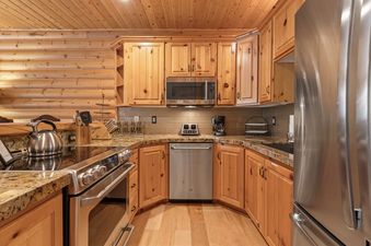 A fully equipped kitchen with wooden cabinetry, stainless steel appliances, and granite countertops is shown.