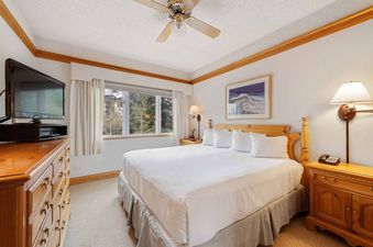 A cozy bedroom with a large bed, wooden furniture, a window with an outdoor view, and a ceiling fan.