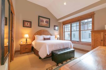 A bedroom with a king-sized bed, wooden nightstands, a mirror, and a large window with a view of the outside.