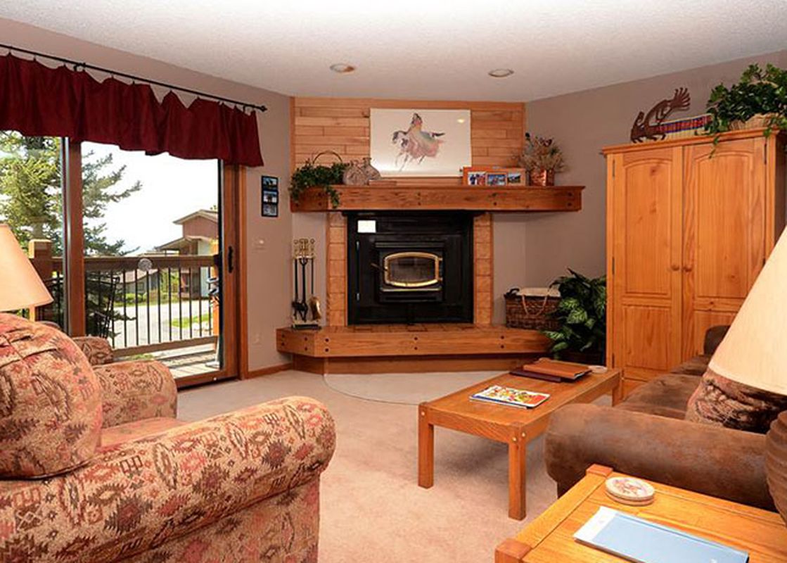 A cozy living room at Ranch at Steamboat RA103 features a fireplace, comfortable sofas, and a sliding glass door leading to a balcony with an outdoor view.