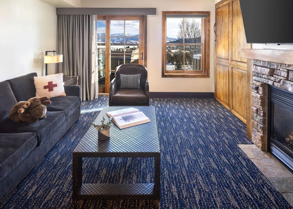 Cozy living area of the Teton Mountain Lodge and Spa Two Bedroom Bi-Level Suite with a stone fireplace, sofa, and mountain view window.