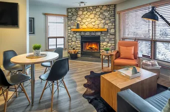 A cozy living room in the Buffalo Mountain Lodge Buffalo Suite, featuring a stone fireplace, comfortable seating, and a dining area, with a winter view through the windows.