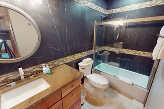 A bathroom with a white toilet, a large oval mirror, and a shower with a glass door.