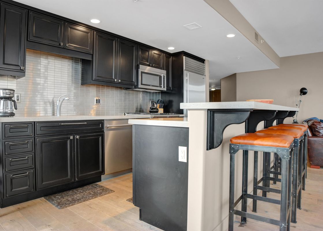 A modern kitchen in Lowell 301B with dark cabinetry, stainless steel appliances, and a breakfast bar with orange leather stools.