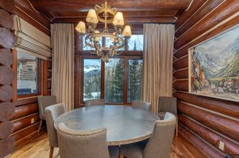 The dining room at Townhomes on the Creek 139 features a round table beneath an ornate chandelier, framed by views of the outdoors.