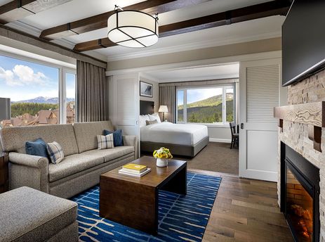 A spacious Fairmont Chateau 2 Bedroom Junior Suite featuring a comfortable living area with a sofa, coffee table, and an ottoman, adjacent to a cozy bedroom with a large bed.