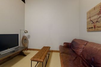 The living room features a leather sofa and an ottoman, a large TV, and a wooden table with a lamp on top.