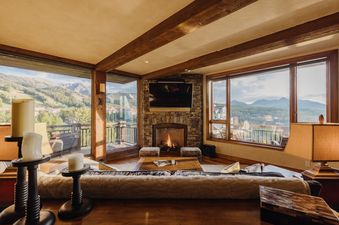 A cozy living room with a fireplace, comfortable seating, and large windows offering panoramic mountain views at Skyline Views at See Forever.