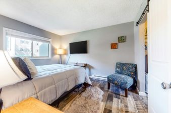 A bedroom with a bed, a chair, a TV, and a door to a closet.