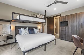 A king-size bed with a dark wooden headboard and a loft bunk above, featuring modern decor and an adjoining bathroom at Nine Peaks.