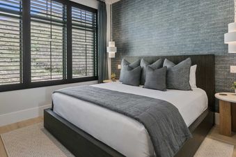 The bedroom at 11981 N Gemini Way SkyRidge features a luxurious bed with white linens and a gray throw, flanked by modern nightstands and pendant lights.