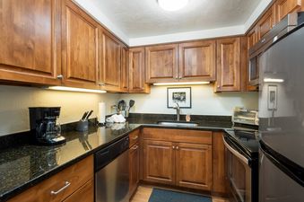 A well-equipped kitchen with wooden cabinetry, black granite countertops, and stainless steel appliances.