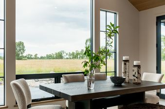 A dining room at Oatgrass Escape features a dark wood table with six chairs, a bench, and a view of golden fields through large windows.