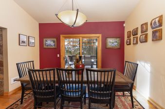 A formal dining room inside Baldy Ridge Chalet with a large wooden table and black chairs, set against a red accent wall and leading to an outdoor deck.