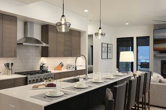 A modern kitchen and living area in Princetown Grande with dark wood cabinetry, stainless steel appliances, a large island with seating, and a fireplace in the adjacent living room.