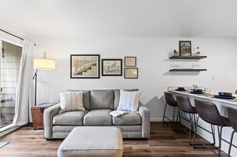 Cozy living space in Snowcrest 207 with a grey sofa, ottoman, and adjacent kitchen bar seating.