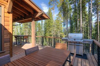 The deck at Moonlight Basin 6 Jakes Lane features a large dining table, a grill, and a view of the forest.