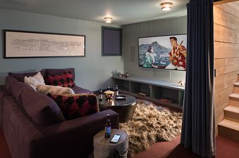 A cozy media room featuring a purple sectional sofa, a large TV on the wall, and a shaggy rug.