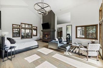 A luxurious open-plan living area with a bed, a fireplace, a black leather sofa, and a patterned armchair, all set against white walls and light wooden floors.