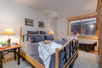 The cozy bedroom at Black Bear 305 Abode features a rustic wooden bed frame, soft lighting, and calming decor.