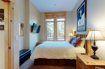 A cozy bedroom in Taylors Crossing 109 with a queen-sized bed, wooden headboard, and a large window overlooking trees.