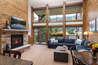 A cozy living room at Montaneros 414 with a fireplace, a large sectional sofa, and expansive windows offering mountain views.