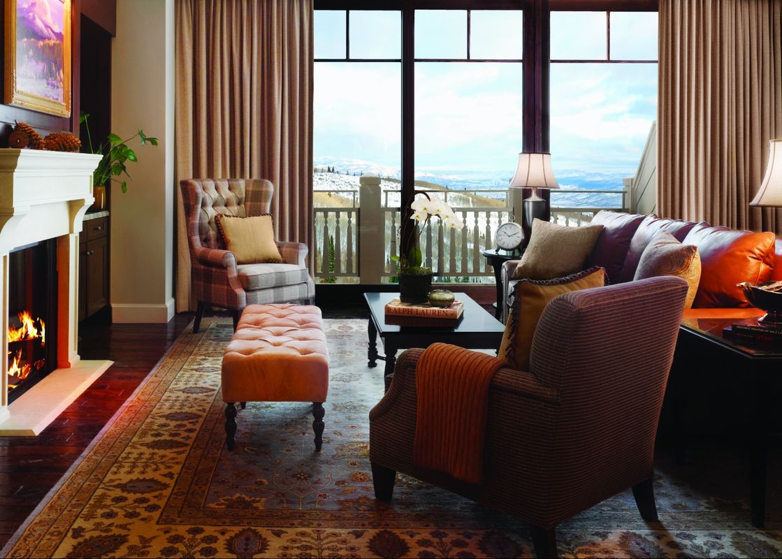 A luxurious and spacious living room, featuring a cozy fireplace, comfortable seating, and large windows with a view of snow-capped mountains.