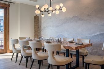 An elegant dining table set for ten with modern cream-colored chairs, a large mountain mural wall, and a striking globe chandelier at the Emerald Mountain One Steamboat Place 702.