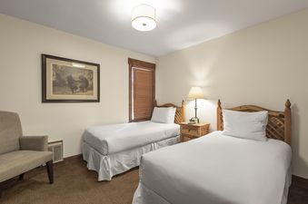 A cozy twin bedroom at Snow Flower 142 Park City with two beds, wooden nightstand, a table lamp, and an artwork of bears on the wall.